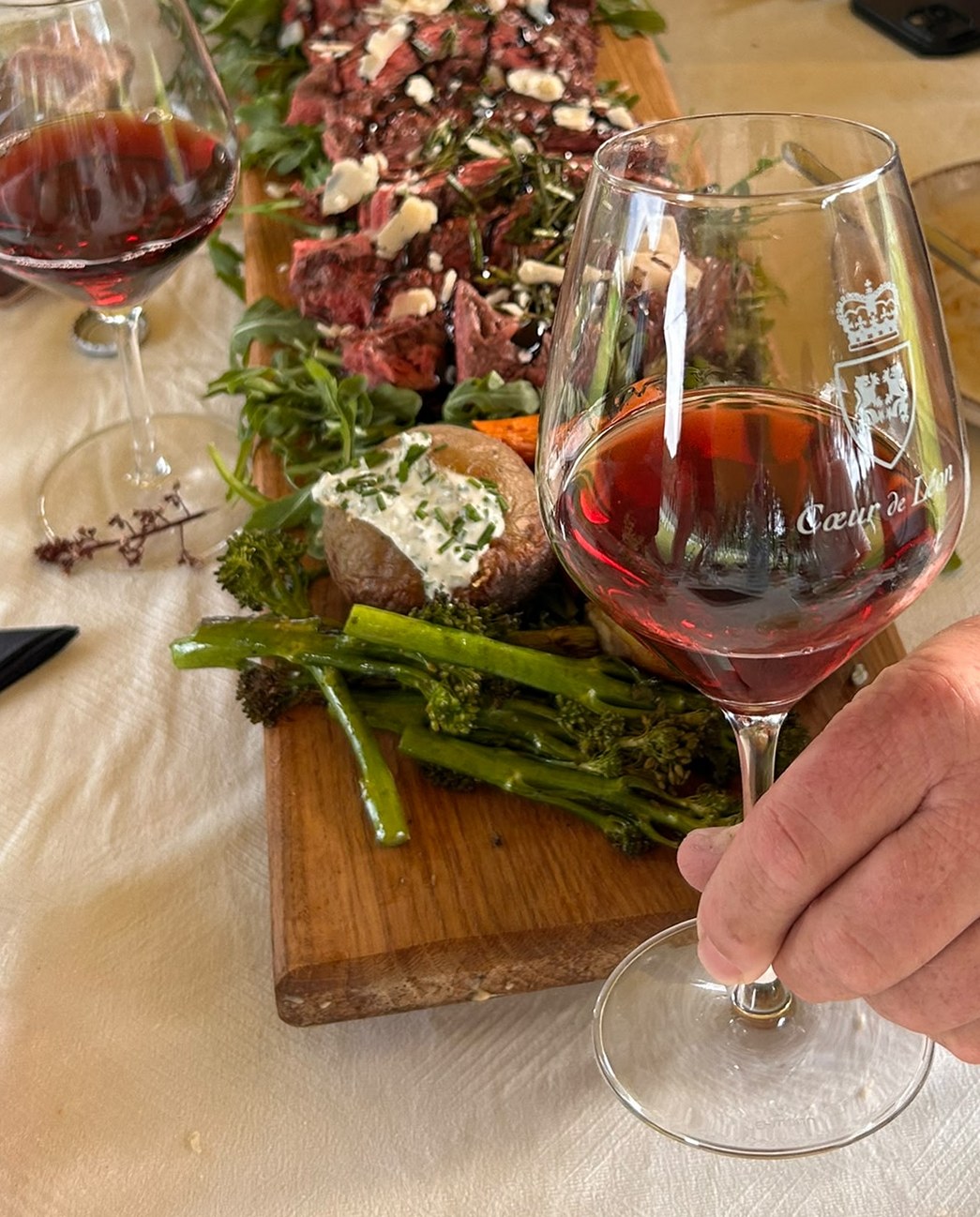 Gast proeft een glas rode wijn aan de gedekte tafel, met de gevulde BBQ-plank op de achtergrond